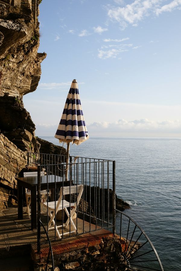 A small terrace table under a striped umbrella, above the sea at Vernazza